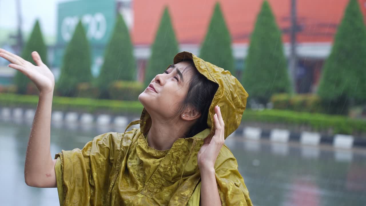 레인코트를 입은 동아시아 여성이 손을 들고 길거리에서 는 동안 아지는 비의 수준을 확인하고, 비가 오는 계절의 준비, 열대 기후 변화, 비에 어지는 것.