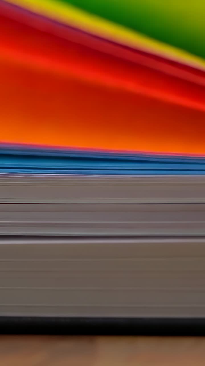 Vídeo vertical: folhas coloridas deslizando e se movendo sobre uma tela neutra na mesa, revelando uma tela encadernada