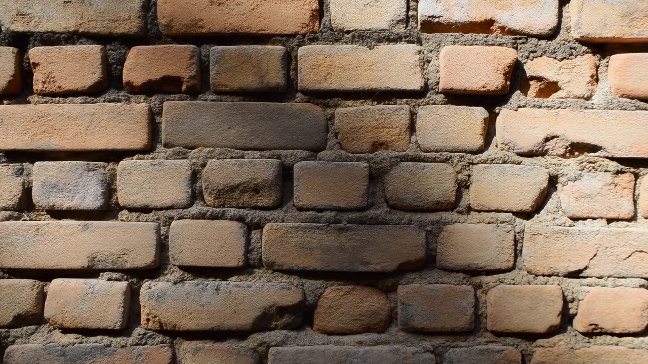 Close view of an aged brick wall with uneven masonry, rough mortar, and warm sunlight creating strong highlights and deep shadows across the surface