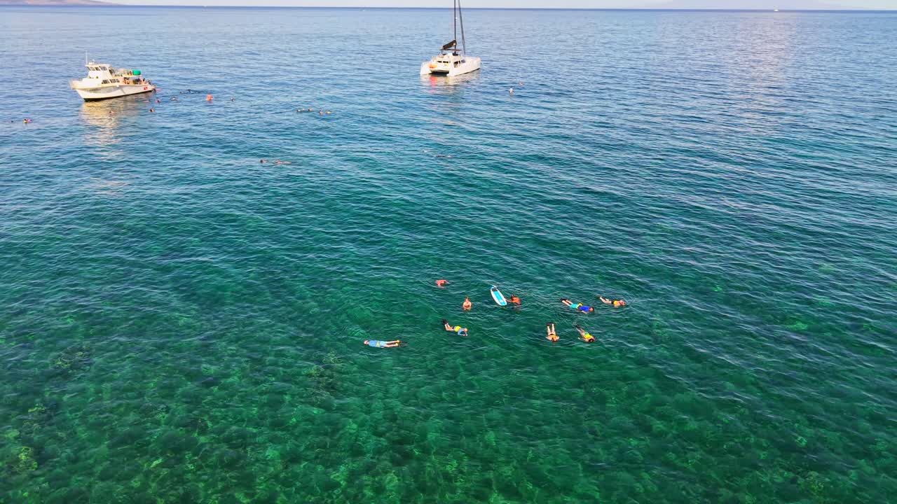 Snorkeling group near tour boats and a catamaran over a coral reef in Maui, aerial shot
