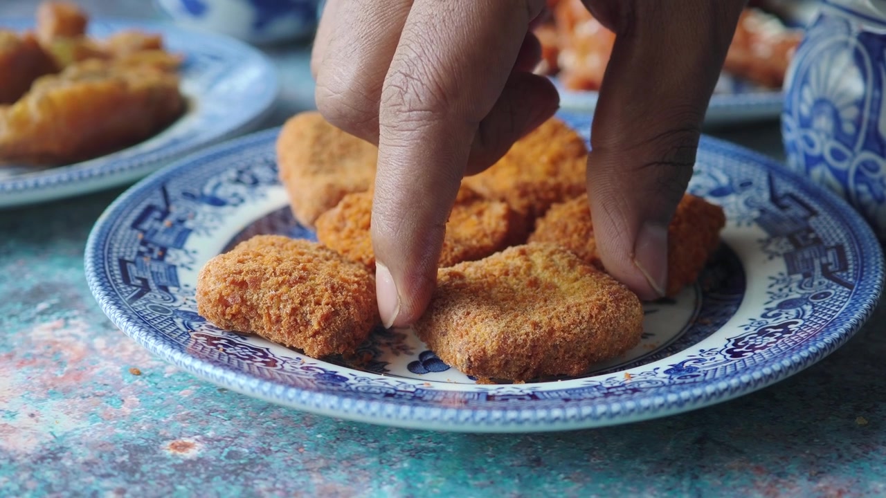 Hand Picking Up a Crispy Fried Chicken Nugget from a Decorative Plate
