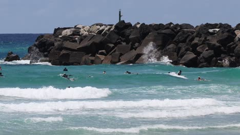 surfers navigating waves near a rocky breakwater