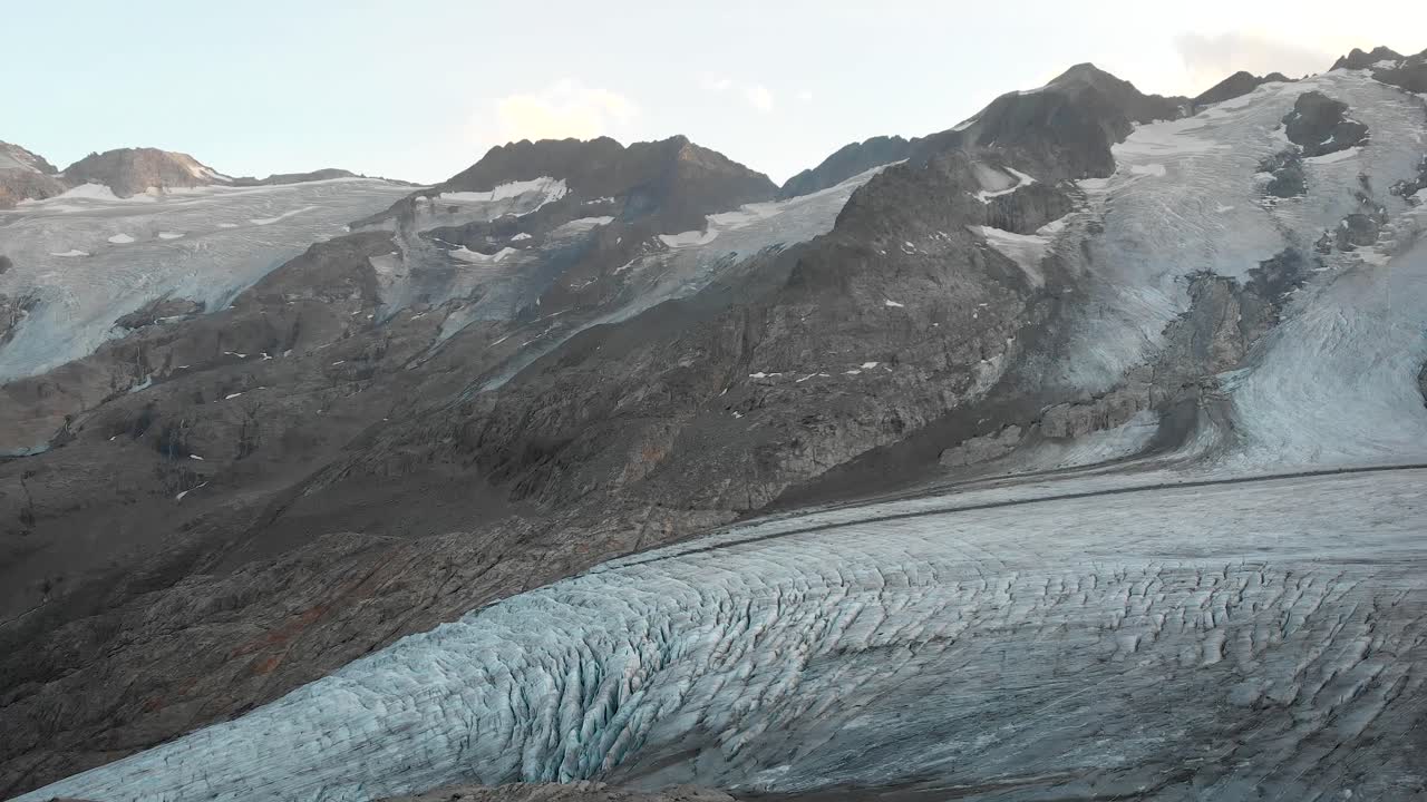 Aerial flight next to the Gauli glacier in the Bernese Oberland region of the Swiss Alps with a panning view over the glacier's crevasses at sunset