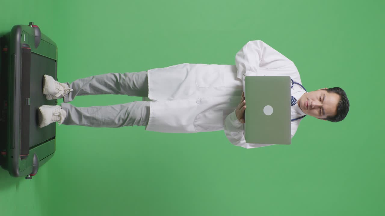 cuerpo lleno de médico masculino asiático con estetoscopio usando una computadora portátil mientras camina en el fondo de la pantalla verde en el hospital