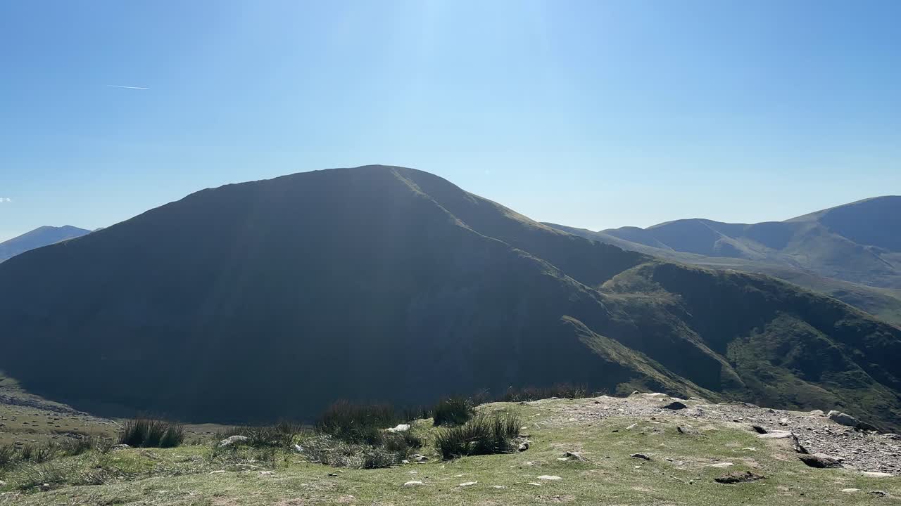 Wide scenic view of peaceful mountain ridge captured from high open ground in Snowdonia National Park with sunlight casting soft shadows over rugged terrain under bright clear sky