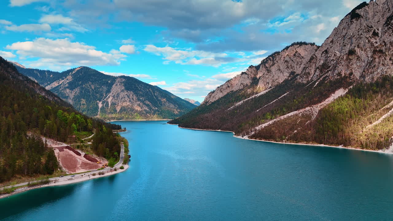 Flight over the peaceful blue waterscape of Lake Plansee flowing among the stunning mountains. Amazing scenery of the nature in Tyrol, Austria.