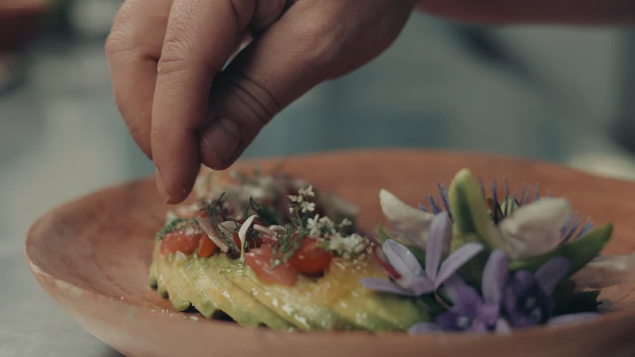 mano del chef poniendo flores en rodajas de aguacate