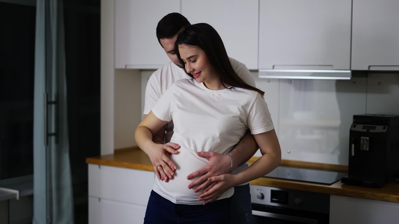 Husband gently stroking pregnant wife tummy indoors in slow motion