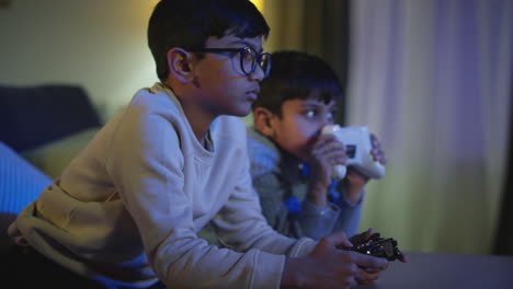 two young boys at home having fun playing with computer games console on tv holding controllers late at night 1