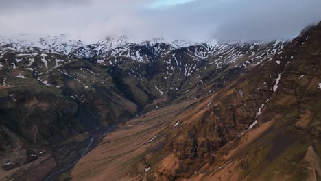 Vista-Aérea-Del-Paisaje-De-Un-Río-Que-Fluye-En-Un-Valle-De-Montaña,-Bajando-De-La-Nieve-Derretida,-En-Islandia,-En-Un-Día-Nublado