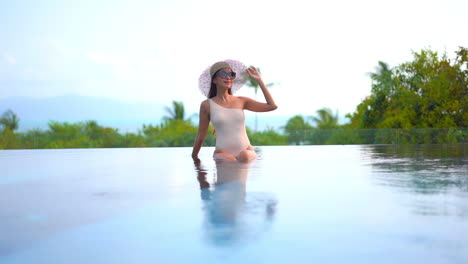 Mujer-Esbelta-Con-Clase-En-Traje-De-Baño-Y-Sombrero-De-Verano-En-El-Borde-De-La-Piscina-Infinita-Del-Complejo-Tropical-Con-Horizonte-Marino-En-El-Fondo,-Cámara-Lenta