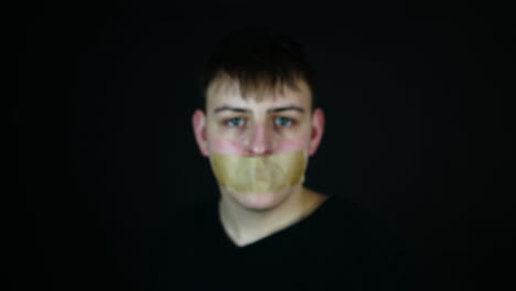 silenced with a tape over mouth, young man showing smartphone with green screen