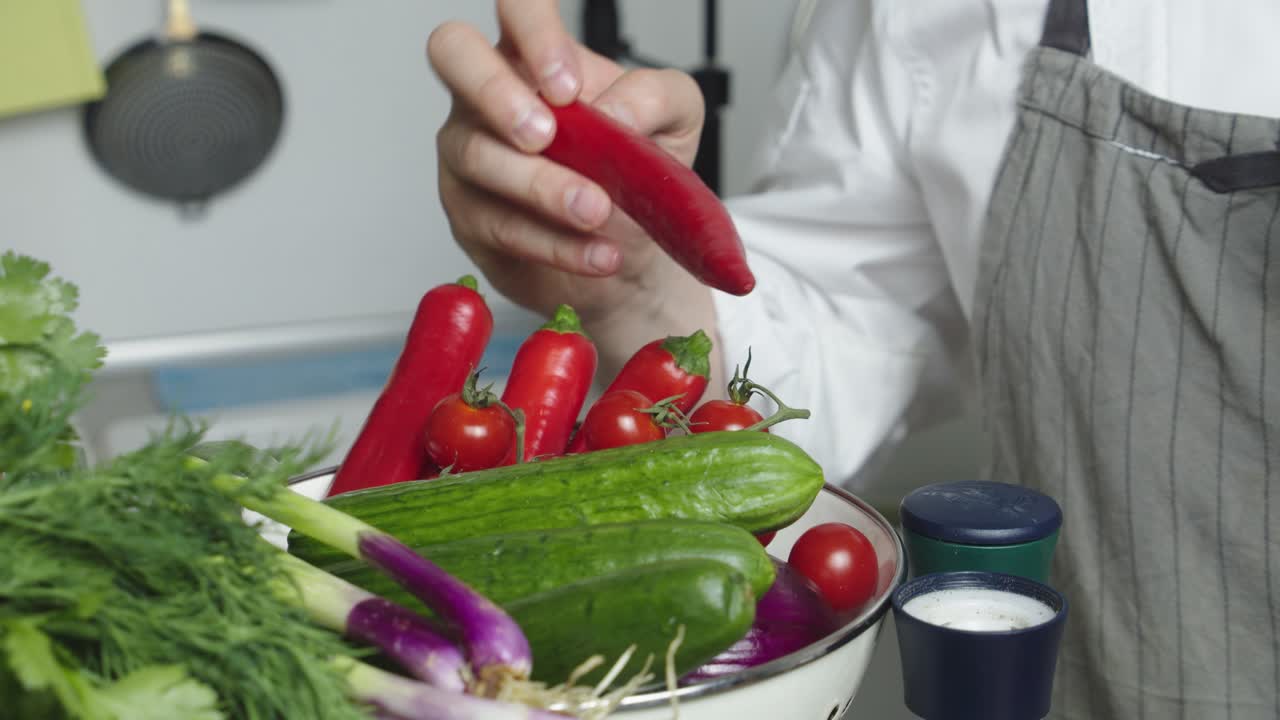 la mano del chef recoge pimiento rojo picante del tazón con verduras en una mesa de cocina
