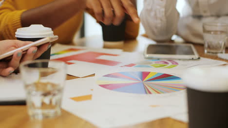 close-up view of hands of multiethnic people pointing graphics on a table in a cafe