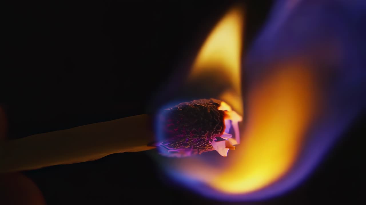 Wooden matchstick igniting with vibrant purple and orange flames, revealing intricate burning patterns and intense colors against dramatic black background