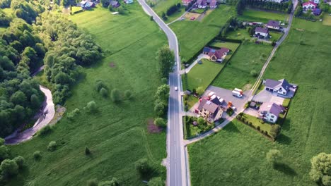 flight over straight road in beautiful scenery, moving cars, houses and green landscape