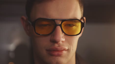 a portrait of a cool guy with yellow eyeglasses smile and blink his eyes in front of camera