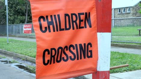 Cerrar-Los-Niños-De-La-Escuela-Naranja-Cruzando-La-Bandera-En-Un-Post