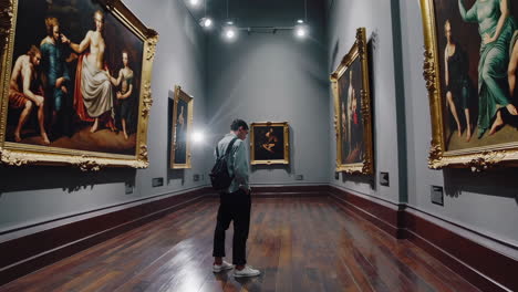 man looking at paintings in a museum