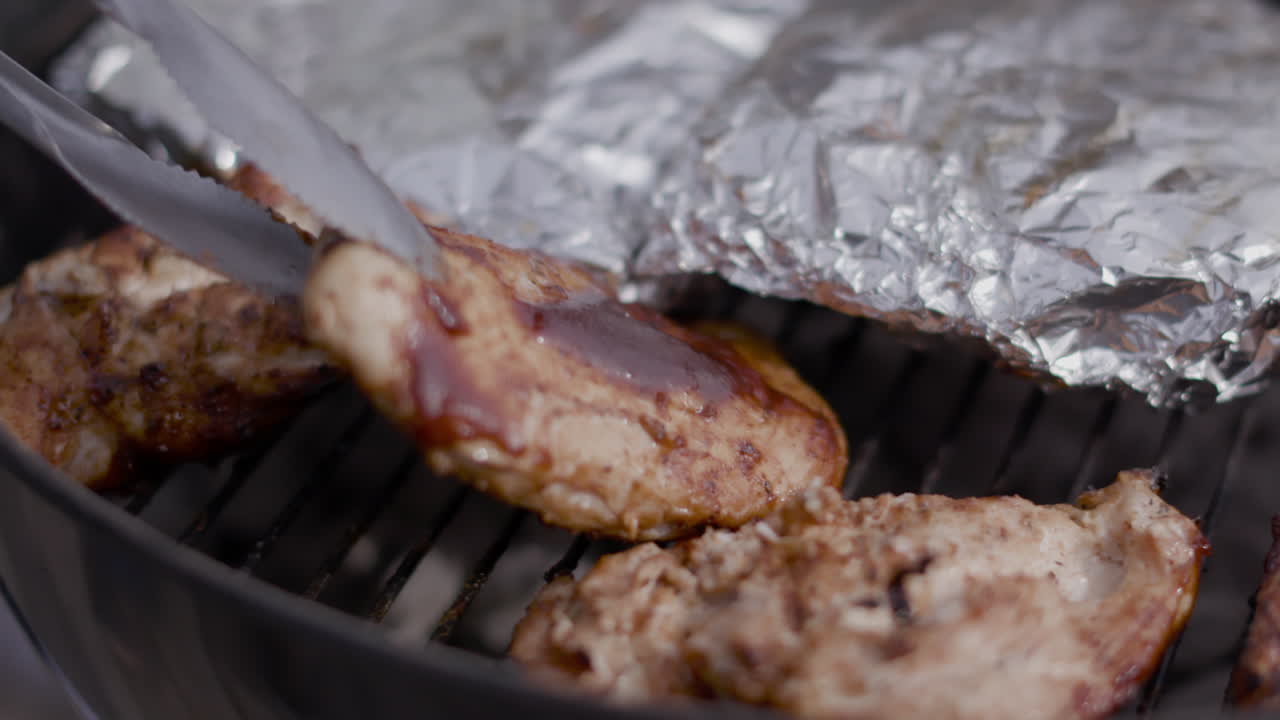 여름에 공공 공원에서 숯불 검은 주전자 그릴에 금속 집게로 바비큐 치킨 뒤집기