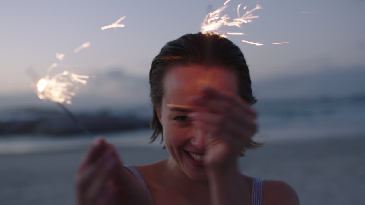 해변에서 춤추는 폭죽을 들고 쾌활한 행복을 느끼는 매력적인 젊은 여성