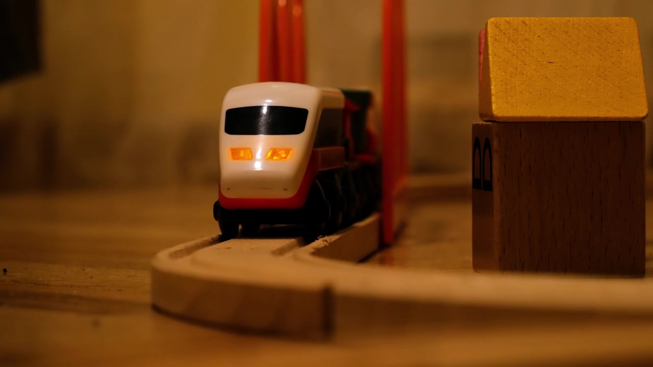 Wooden toy train track and small house with warm lighting.