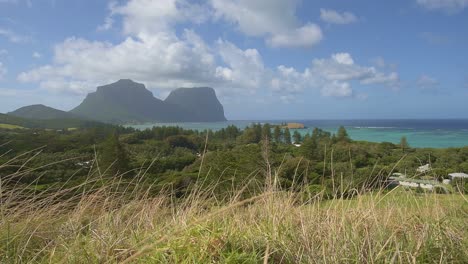 Mirando-Hacia-La-Isla-De-Lord-Howe-En-Un-Día-Soleado-Con-Hierba-Seca-Doblada-Por-El-Viento-En-Primer-Plano-Y-Mt-Gower-En-El-Fondo