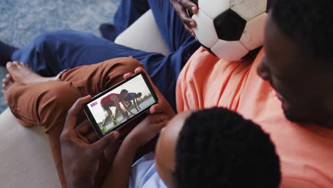 Composite-of-father-and-son-at-home-watching-athletics-running-event-on-smartphone