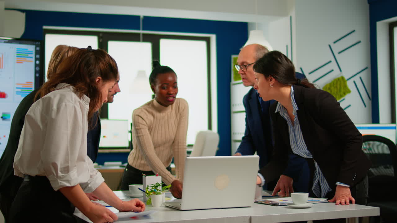 Multicultural workers group talking, looking at laptop and analyzing digital datas