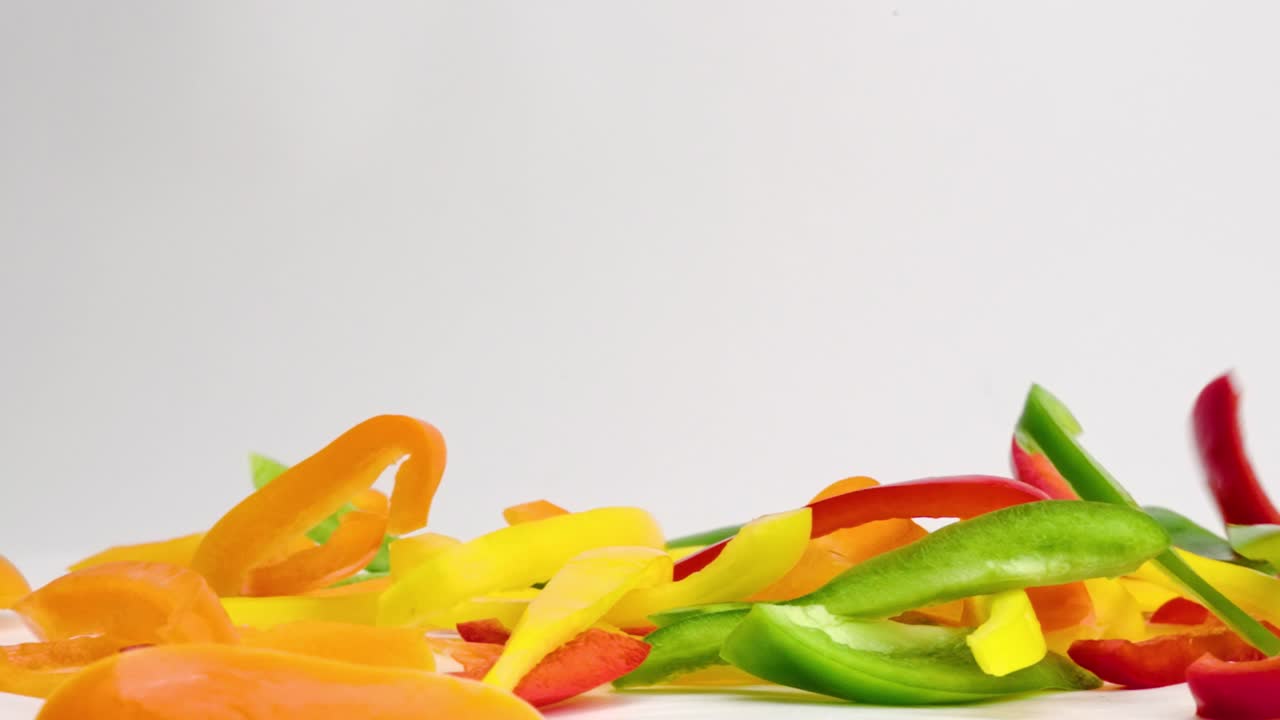 mezcla de verduras de pimiento de colores brillantes cayendo y rebotando en una pila en la parte superior de la mesa blanca en cámara lenta