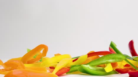 bright colorful bell pepper vegetable medley falling and bouncing into a pile on white table top in slow motion