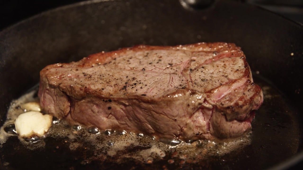 Bistecca succosa che sfrigola nel burro con aglio. Carne di manzo che cuoce in una padella di ghisa.