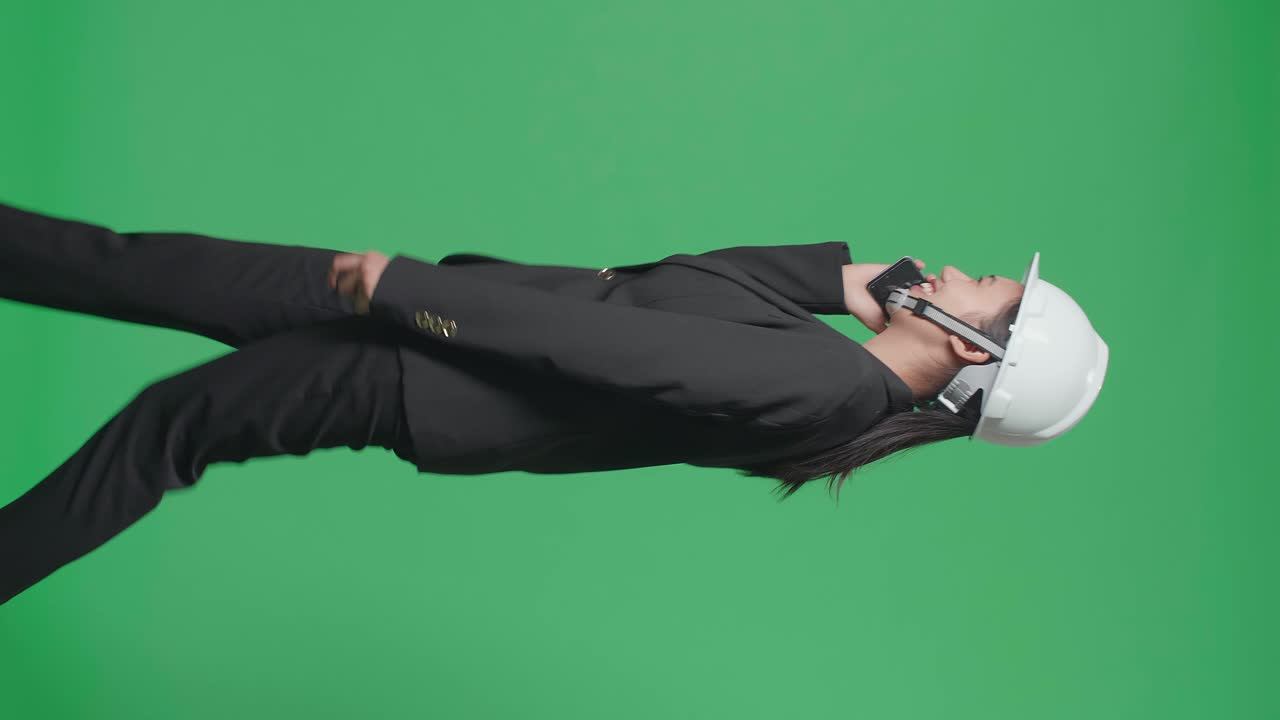 Side View Of Smiling Asian Female Engineer Talking On Smartphone And Walking In The Green Screen Studio