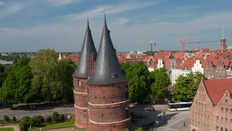 Aerial-orbit-shot-around-Holstentor,-medieval-town-gate.-Big-church-Marienkirche-with-two-green-towers-in-background.-Luebeck,-Schleswig-Holstein,-Germany