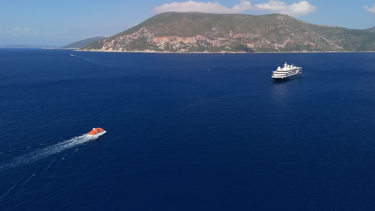 Droneudsigt over en tenderbåd, der vender tilbage til et krydstogtskib ankret op ud for en græsk ø om sommeren.