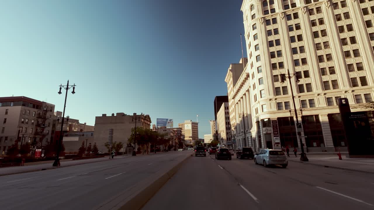 POV shot of car driving through intersection in historic downtown with vintage buildings and clear blue sky