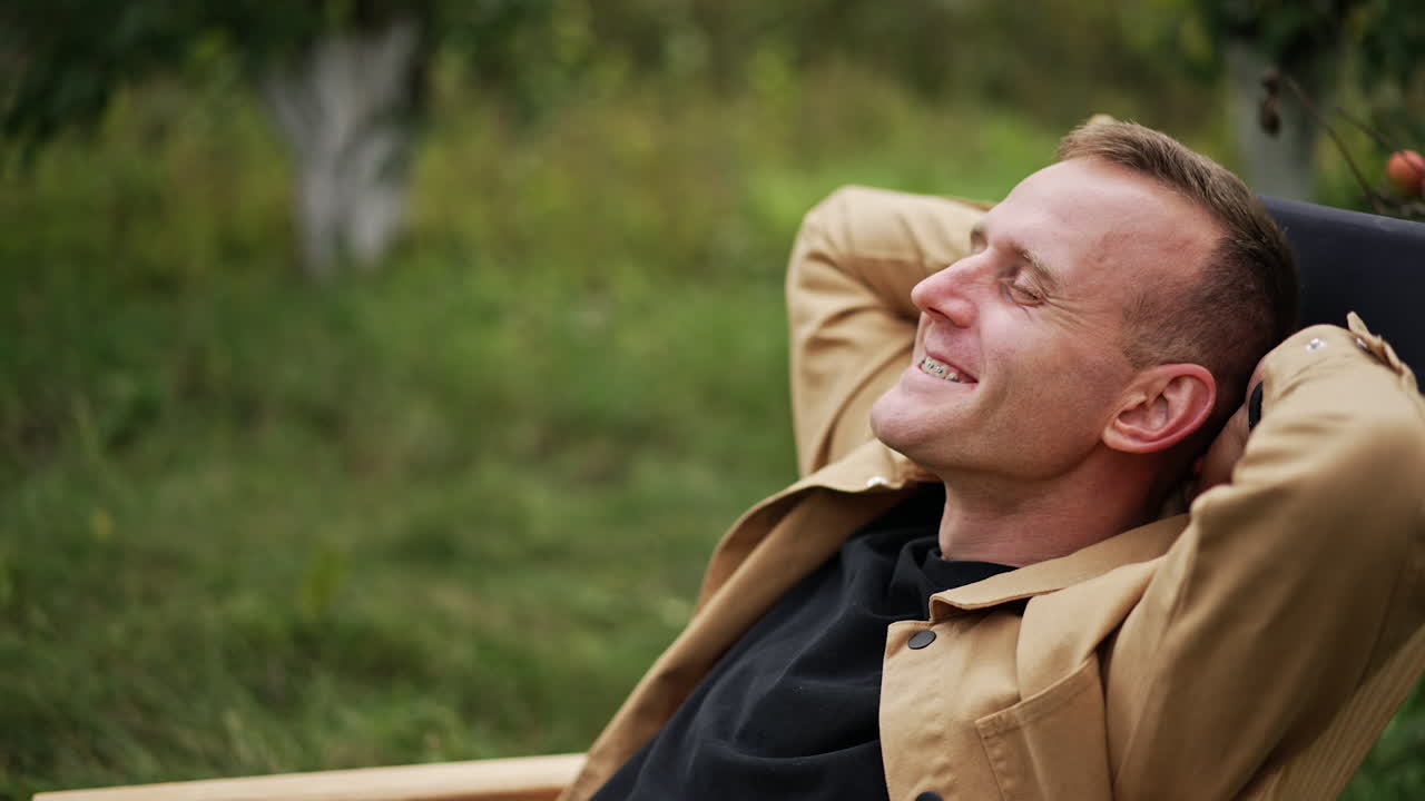 Happy smiling resilient man sitting in the chair outdoors. Male freelancer opens laptop and starts his remote online work. Nature backdrop.