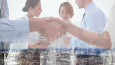 mid section of businessman and businesswoman shaking hands at office over aerial view of cityscape