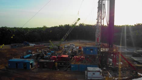 Cinematic-4K-Drone-Footage-of-Onshore-Drilling-Rig-equipment-structure-for-oil-exploration-and-exploitation-in-the-middle-of-jungle-surrounded-by-palm-oil-trees-during-sunset-and-high-oil-price