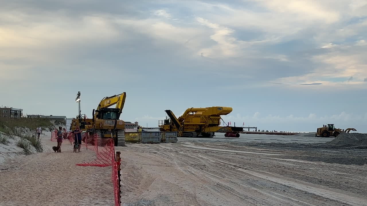 People walking by construction equipment at beach sand replenishment