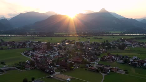 aerial view over a summer forest during sunrise with mountain landscape in the austrian alps with houses in a small town in the background