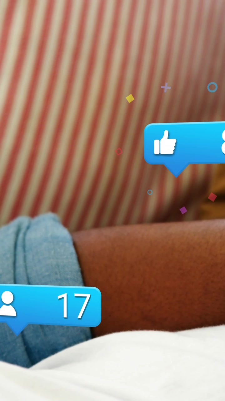 Animation of social media icons over rear view of african american man using smartwatch at home