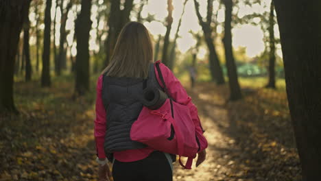 woman walking with a yoga mat through an autumn park