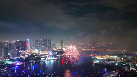 fireworks explode in dazzling rhythm with glittering city lights and anchored boats creating a stunning canvas beneath