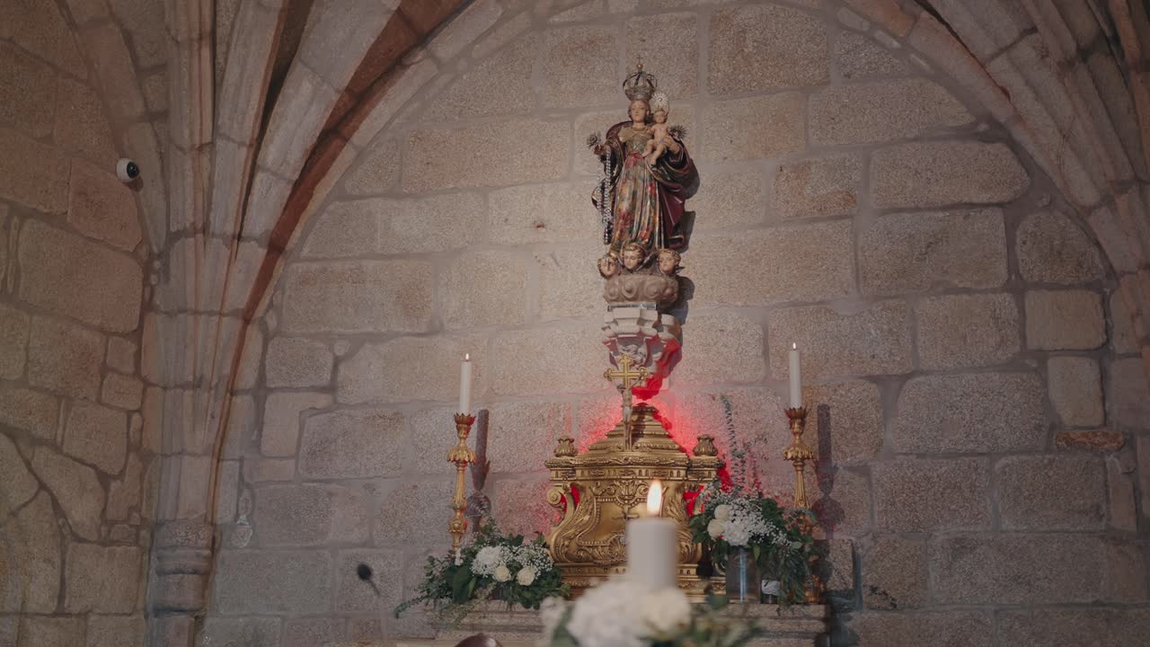 altar ornamentado con estatua y velas rodeado de flores dentro de una capilla antigua