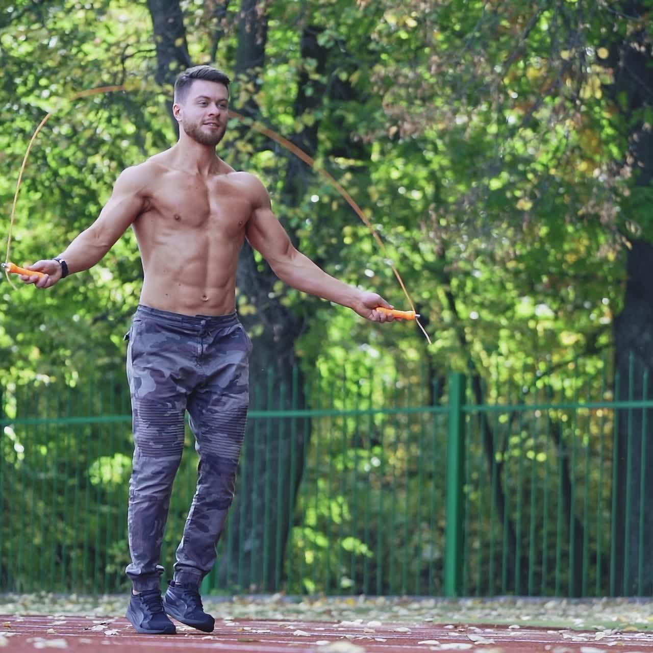 Fitness sportsman jumping with skipping rope. Muscular athlete doing exercise on rope on the outdoor stadium. Slow motion.