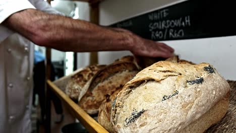 baker places fresh out the oven sourdough loaves onto a shelf for sale in a bakery