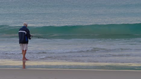 an old man catching fish with a fishing rod at the coast - wave rolling ashore in currumbin beach - fishing in gold coast, qld, australia - wide shot