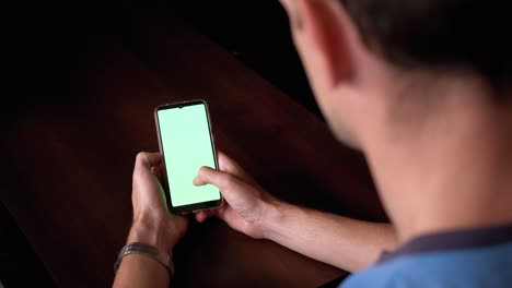 hombre desliza los dedos sobre el centro de un teléfono inteligente con una pantalla verde en la oscuridad