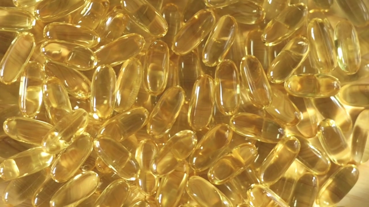 Primo piano di capsule dorate di omega-3 impilate, che evidenziano la loro consistenza liscia e l'aspetto traslucido sotto una luce brillante